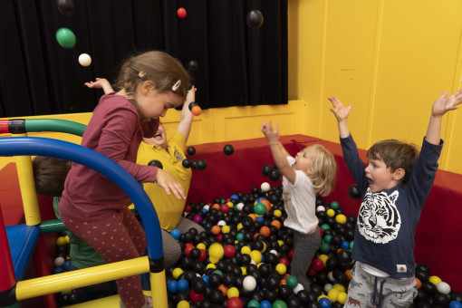 Drei Kinder spielen im Bällebad und werfen Bälle in die Luft