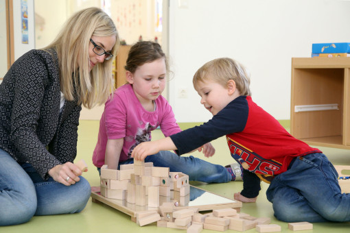 Zwei Kinder bauen mit der Pädagogin ein Gebäude aus Holzbausteinen