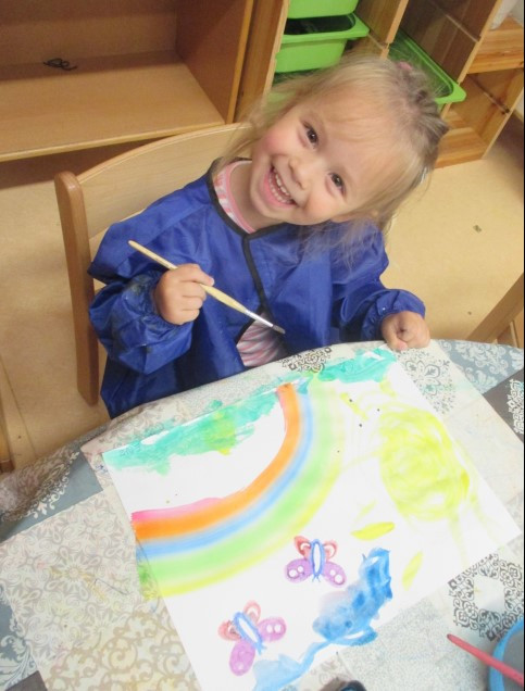 Ein Mädchen gestaltet glücklich ein Bild mit Wasserfarben