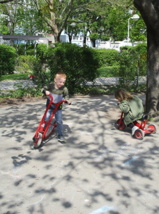 Zwei Kinder düsen mit Tretfahrzeugen durch den Garten 