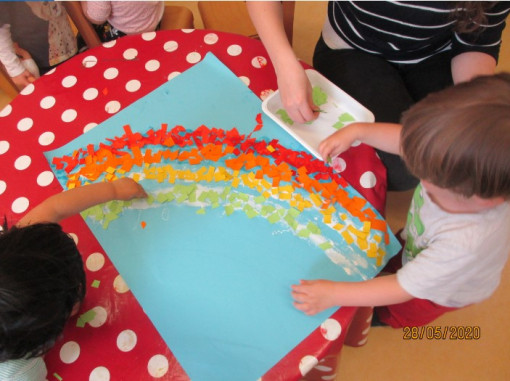 Kinder gestalten, mit ihrer Pädagogin gemeinsam, einen Regenbogen aus Papierschnipseln 