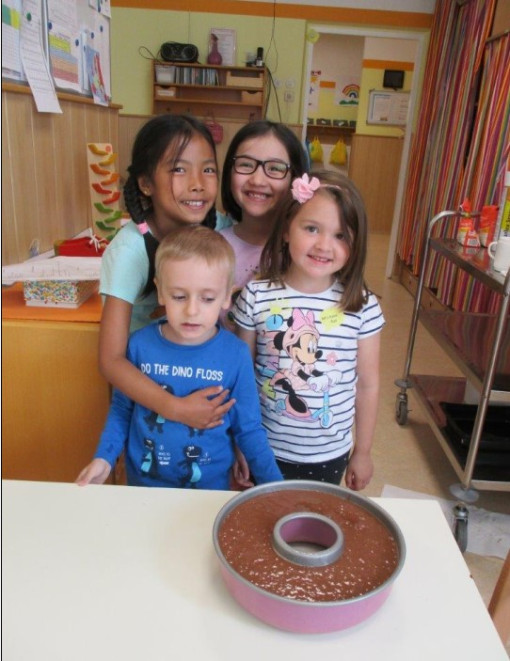 Vier Kinder posieren stolz vor einem Kuchen den sie gemeinsam mit der Pädagogin gebacken haben