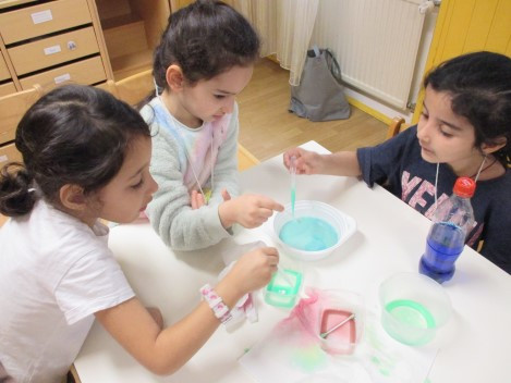 Drei Mädchen führen Farbexperimente durch mit bunten Flüssigkeiten